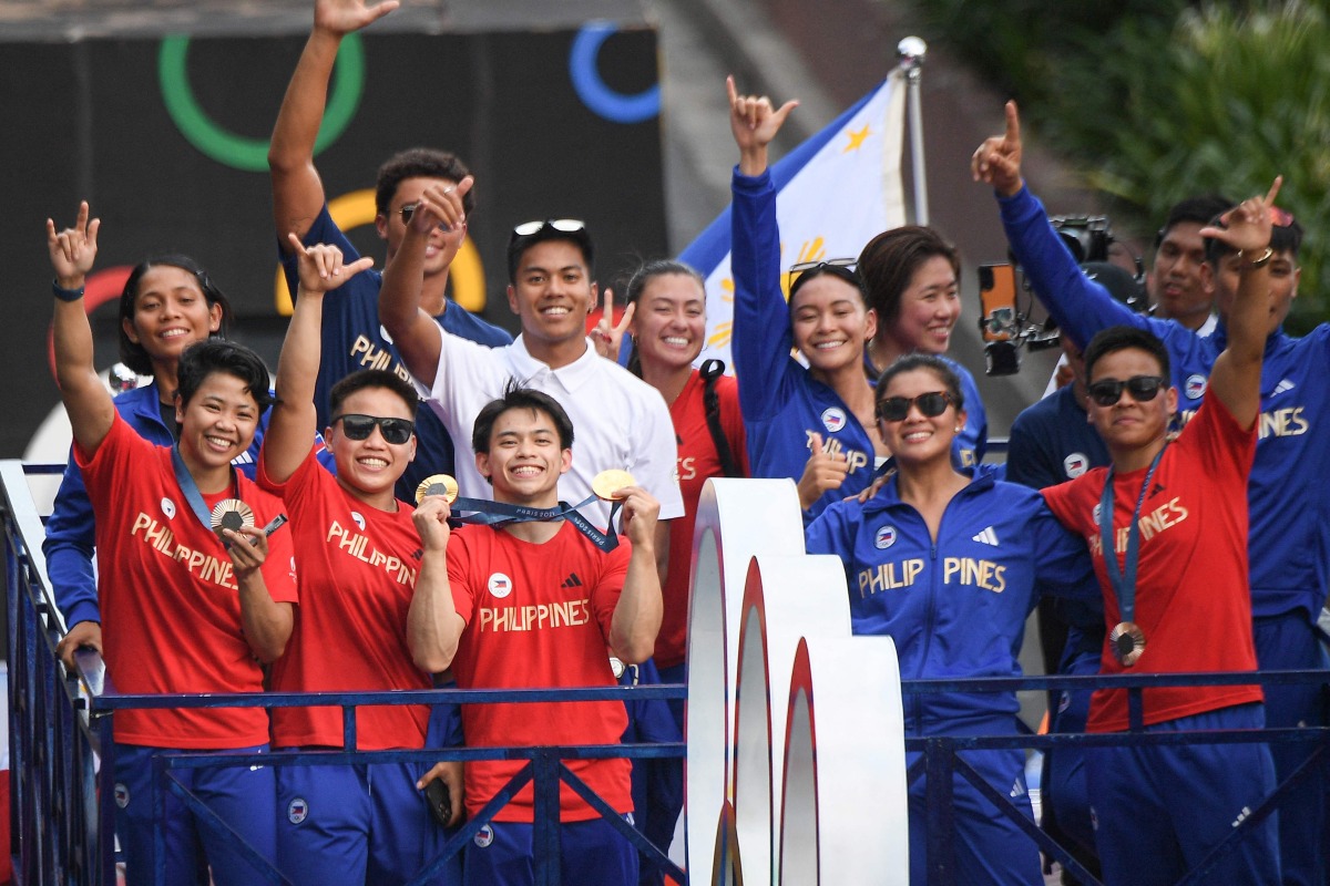 Philippines' Carlos Yulo (C), Paris 2024 Olympic Games double gold medalist in gymnastics, and other Philippine athletes who competed at Paris 2024 Olympics, wave from a float during a celebratory homecoming parade along a street in Manila on August 14, 2024. (Photo by Ted ALJIBE / AFP)