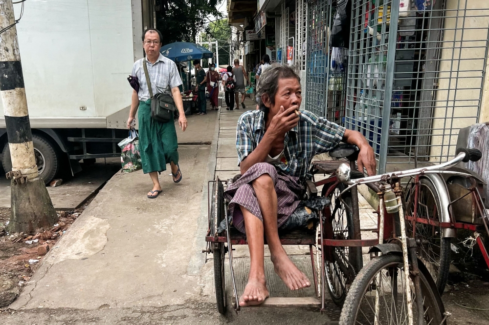 A trishaw driver smokes as he waits for passengers in Yangon on August 13, 2024. (Photo by Saiaung Main / AFP)
