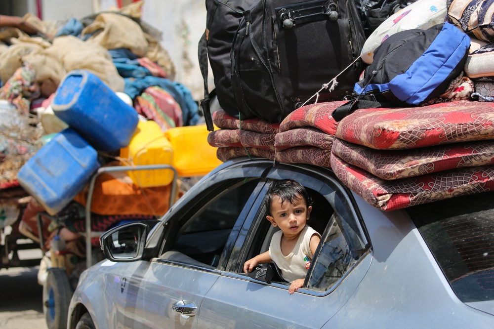 A child peeks out from the window of a car as Palestinians flee with their belongings Deir el-Balah in the central Gaza Strip on August 16, 2024. (Photo by Eyad Baba / AFP)