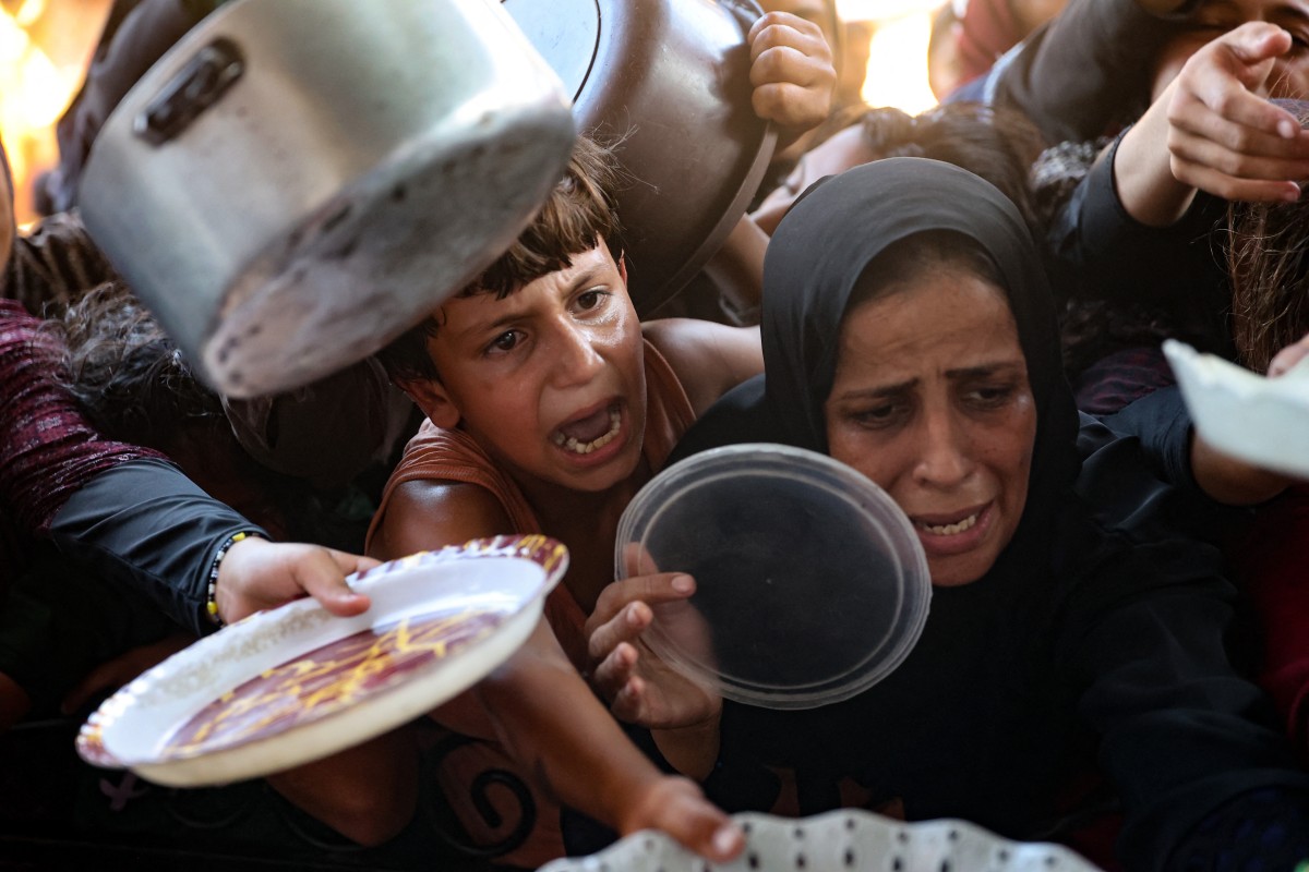 Palestinian women and children hold out their plates toward a man, to receive their share of vegetable patties prepared by volunteers in Beit Lahia in the northern Gaza Strip on August 14, 2024. Photo by Omar AL-QATTAA / AFP.