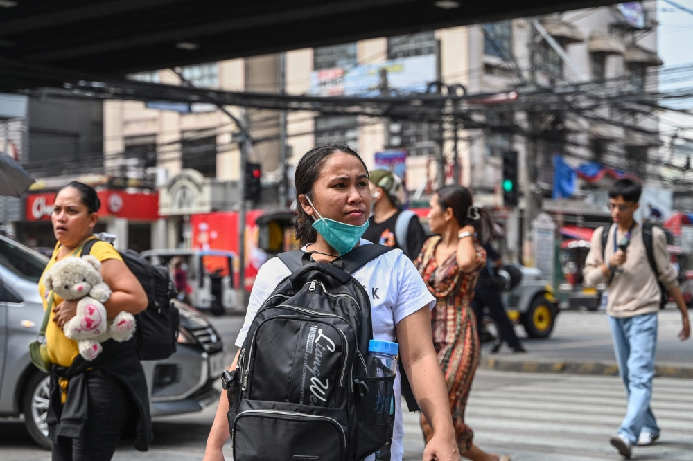 A woman wearing a face mask crosses a street with other people in Manila on August 21, 2024. (Photo by Jam Sta Rosa / AFP)