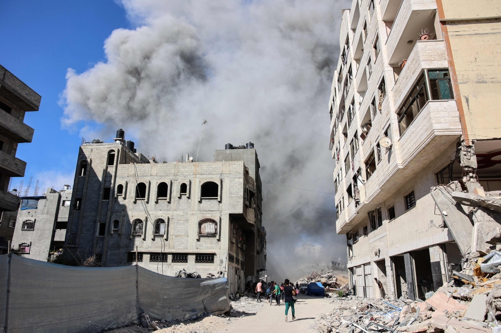 Palestinians watch as smoke rises from a building hit by an Israeli strike after a warning from the army to its occupants to evacuate the premises, in the Rimal neighbourhood of central Gaza City on August 21, 2024. (Photo by Omar Al-Qattaa / AFP)
 