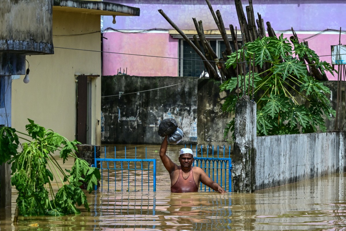 A man carrying his belongings wades through flood waters in Feni, in south-eastern Bangladesh, on August 23, 2024. Photo by MUNIR UZ ZAMAN / AFP.