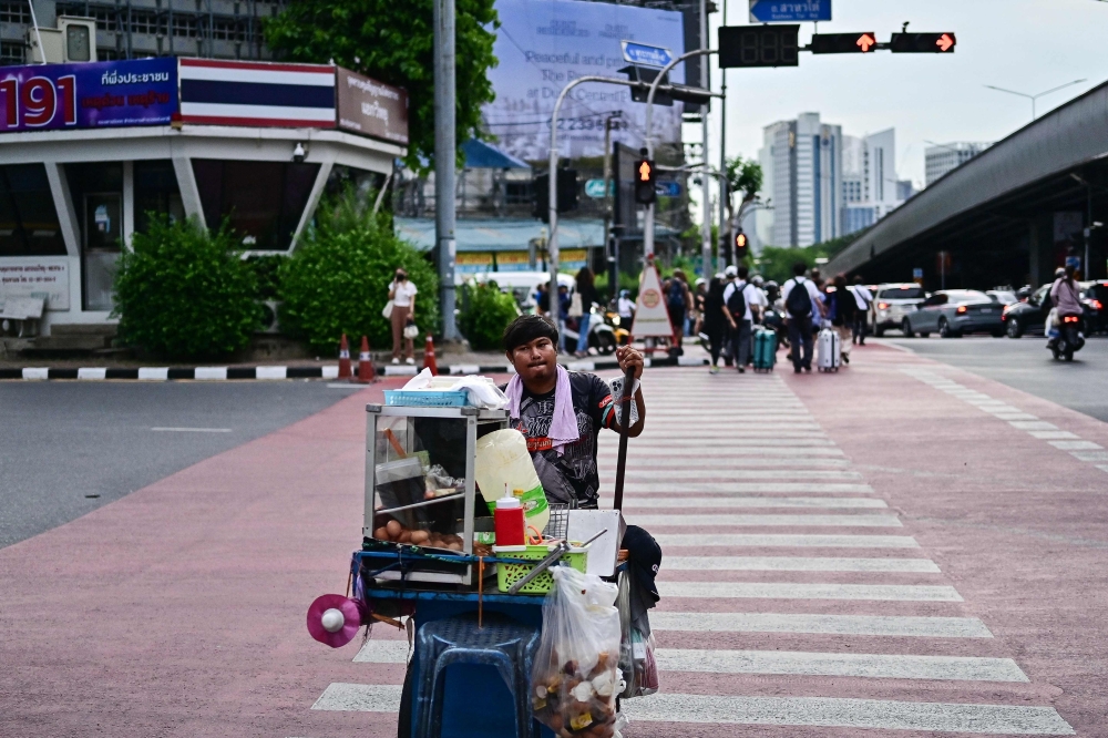 A vendor pushes his cart as he crosses a street in Bangkok on August 23, 2024. (Photo by MANAN VATSYAYANA / AFP)