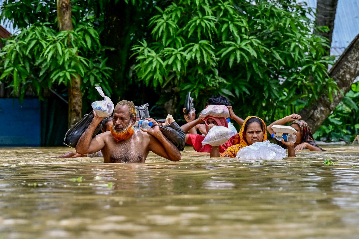 People carrying relief materials wade through flood waters in Feni, in south-eastern Bangladesh, on August 24, 2024. Photo by Munir Uz Zaman / AFP.