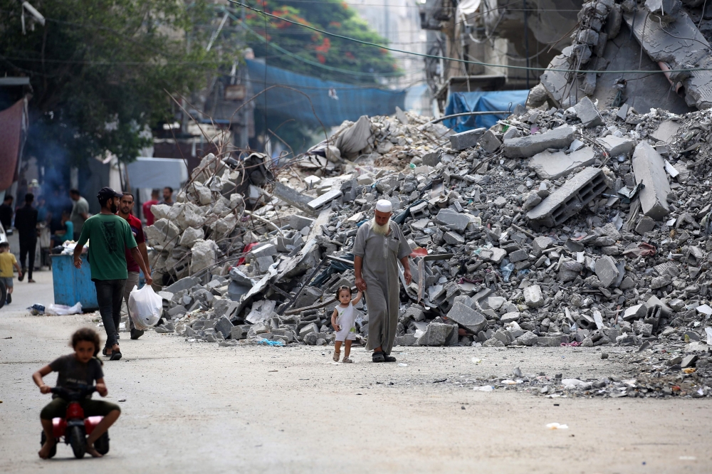 An elderly man holds a child by the hand as he walks past a building levelled by Israeli bombardment in the Bureij refugee camp in central Gaza Strip on August 25, 2024. (Photo by Eyad Baba / AFP)