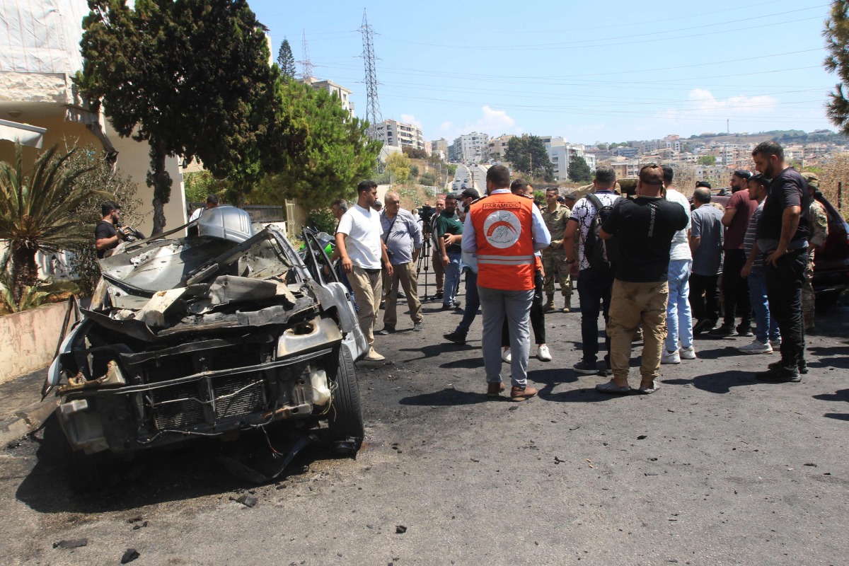 Lebanese security and emergency personnel gather around a burnt car that was reportedly targeted in an Israeli drone strike in the Abra area of the southern city of Sidon, on August 26, 2024. (Photo by Mahmoud ZAYYAT / AFP)
