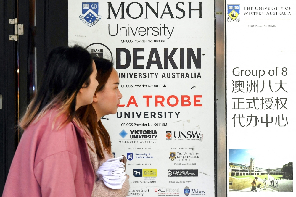 Women walk past signage advertising Australian universities in Melbourne's central business district on June 10, 2020. Photo by William WEST / AFP