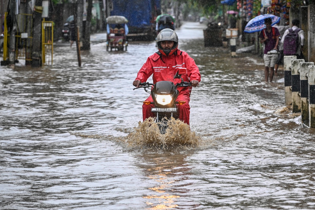 A man riding a motorbike moves through a flooded street after heavy rainfall during monsoon in Guwahati on August 20, 2024. Photo by Biju BORO / AFP.
