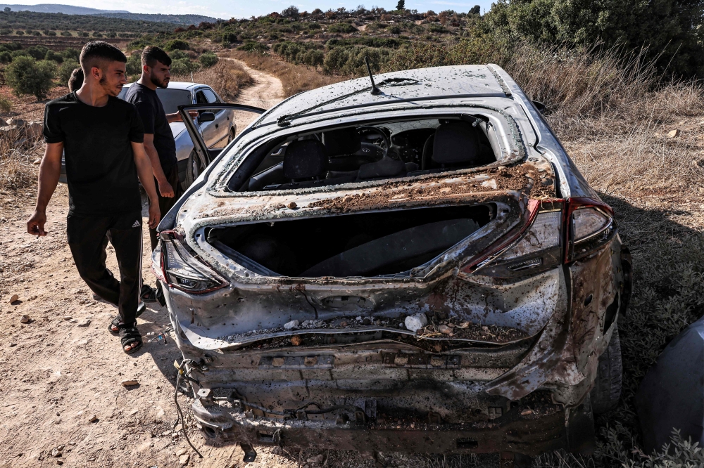 People inspect a destroyed vehicle after an Israeli army raid along a road between Jenin and Tubas in the north of the occupied West Bank on August 28, 2024. (Photo by Zain JAAFAR / AFP)
