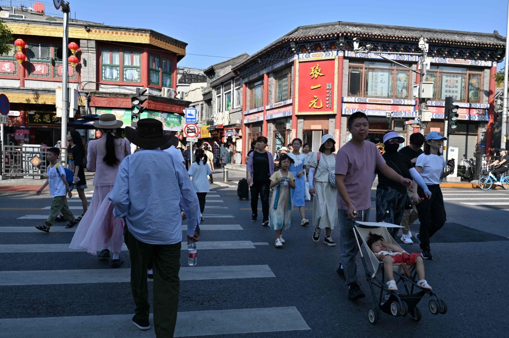 People cross a street in Beijing on August 29, 2024. (Photo by ADEK BERRY / AFP)