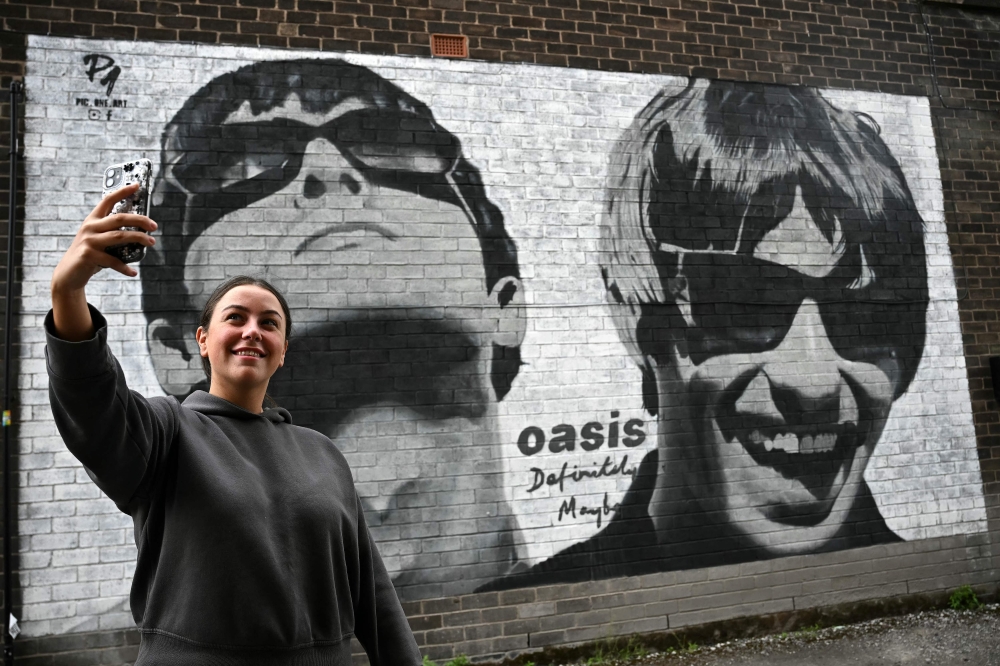 Fan Emily McShane, takes a photograph of a new street artwork depicting Oasis' Liam and Noel Gallagher, created by Manchester-based street artist Pic.One.Art. on the side of the Sifters Record store in Burnage, a suburb of Manchester, north-west England on August 27, 2024. Photo by Paul ELLIS / AFP