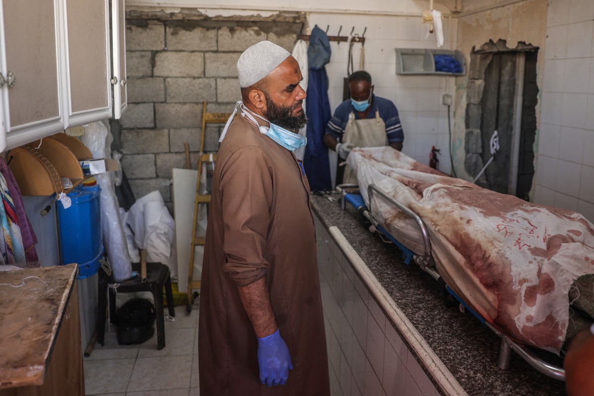 A Palestinian worker stands at a morgue near a body in a hospital following Israeli bombardment, on September 7, 2024. Photo by Eyad BABA / AFP.
