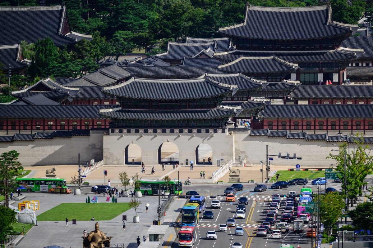 People walk past Gyeongbokgung Palace as people drive their vehicles along a main road past a statue of King Sejong (bottom L) at Gwanghwamun Square in Seoul on August 30, 2024. (Photo by ANTHONY WALLACE / AFP)
