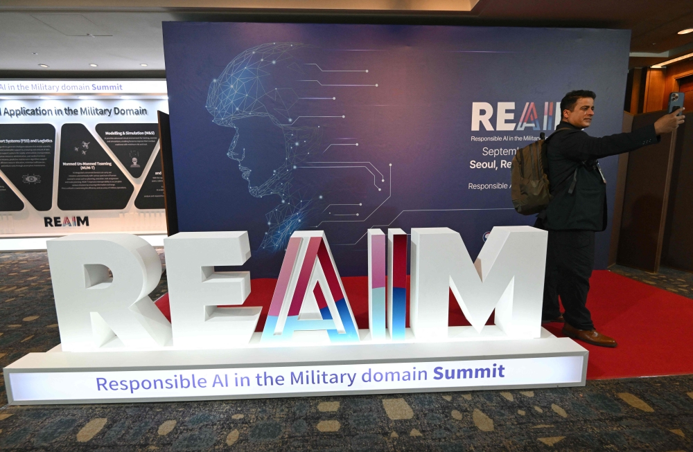 A participant takes a selfie in front of the logo of the Responsible AI in the Military Domain (REAIM) summit before its closing session in Seoul on September 10, 2024. (Photo by Jung Yeon-je / AFP)