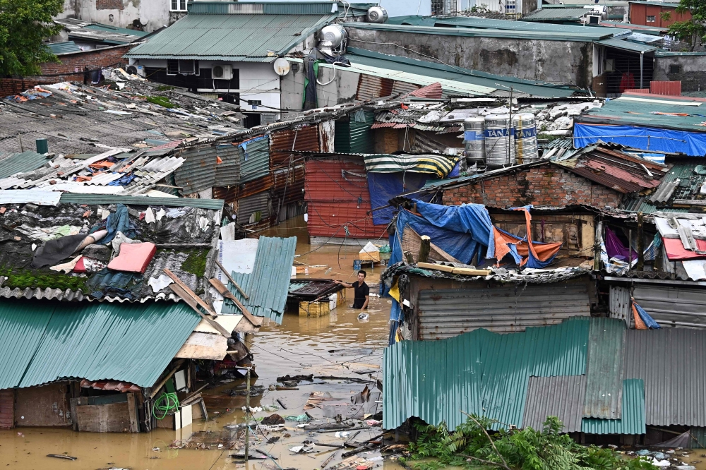 A man walks through floodwaters past partially submerged houses in Hanoi on September 10, 2024, after typhoon Yagi hit Vietnam. Photo by Nhac NGUYEN / AFP