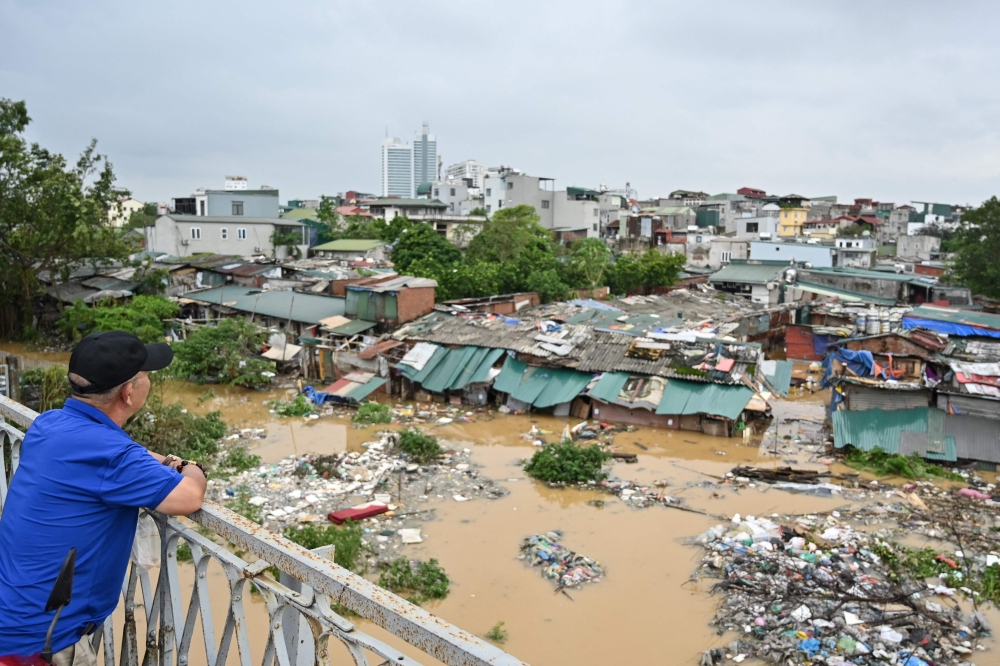 A man standing on Long Bien Bridge looks down at houses partially submerged in floodwaters in Hanoi on September 10, 2024, after typhoon Yagi hit Vietnam. Photo by Nhac NGUYEN / AFP