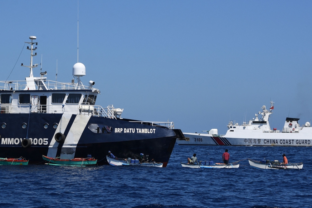 File: This photo taken on February 15, 2024 shows Filipino fishermen aboard their wooden boats, as a Chinese coast guard ship monitors near the China-controlled Scarborough Shoal, in disputed waters of the South China Sea. (Photo by Ted Aljibe / AFP)

