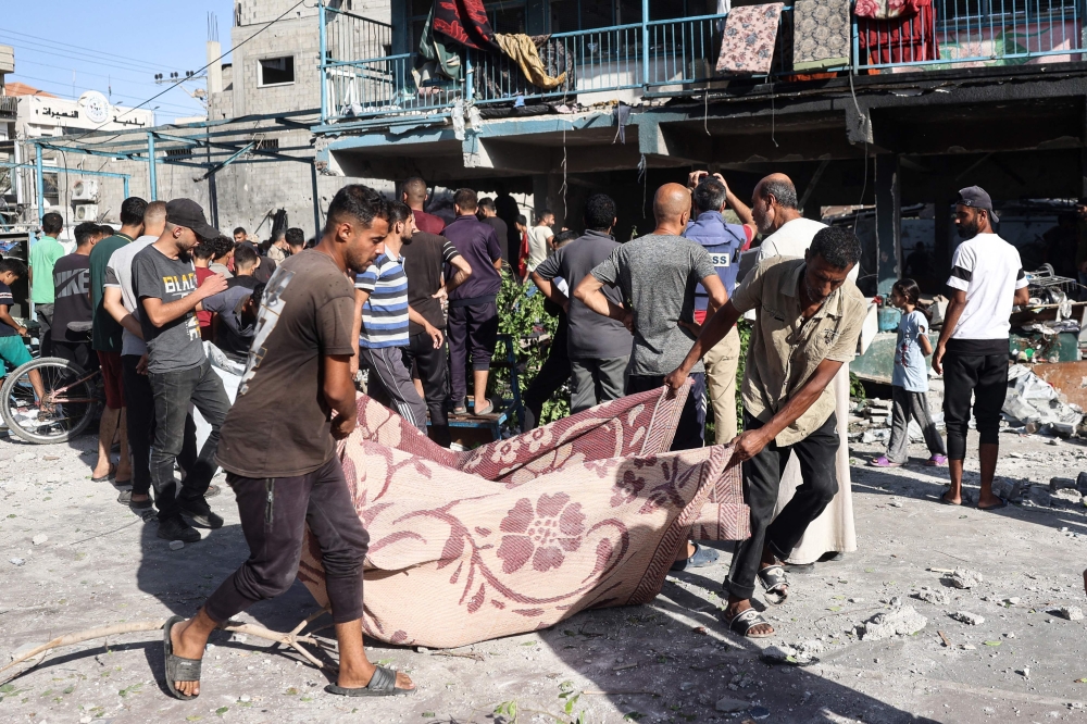 People use a blanket to transport a victim after an Israeli air strike hit a school in Nuseirat, in the central Gaza Strip on September 11, 2024. (Photo by Eyad Baba / AFP)