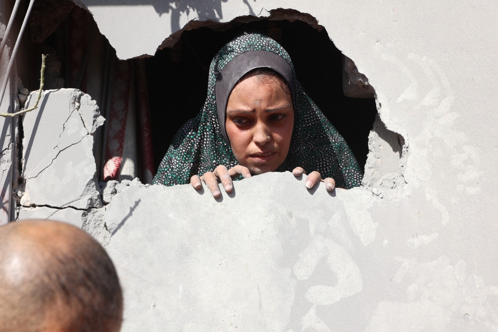 A Palestinian woman looks out through a hole in her home after an Israeli strike in the Shejaiya suburb east of Gaza City on September 12, 2024. (Photo by Omar Al-Qattaa / AFP)