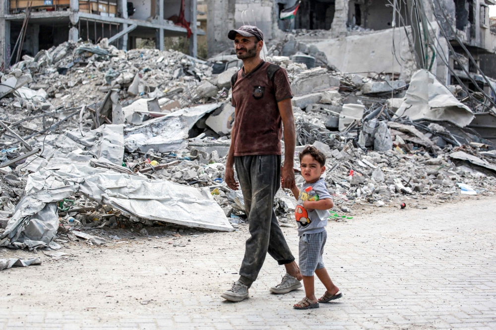 A man and child walk past the rubble of a collapsed building in Khan Yunis in the southern Gaza Strip on September 16, 2024 amid the ongoing war in the Palestinian territory between Israel and Hamas. (Photo by Bashar Taleb / AFP)