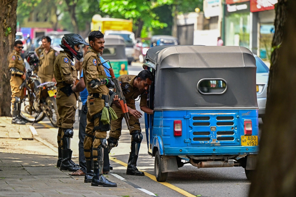 Sri Lankan police combat officers inspect an auto-rickshaw at a road checkpoint ahead of the upcoming presidential elections, in Colombo on September 19, 2024. (Photo by Ishara S Kodikara / AFP)