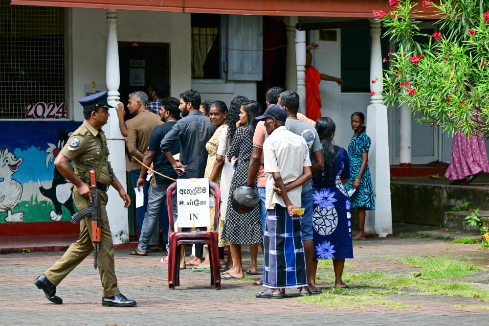 People wait in a queue to cast their ballots at a polling station as police keep watch during voting in Sri Lanka's presidential election in Colombo on September 21, 2024. (Photo by Ishara S. Kodikara / AFP)