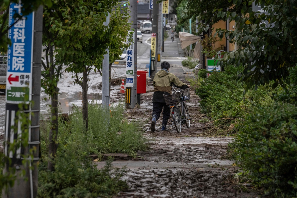 A man pushes his bicycle along a muddy sidewalk following heavy rain in Wajima city of Ishikawa prefecture on September 22, 2024. (Photo by Yuichi Yamazaki / AFP)