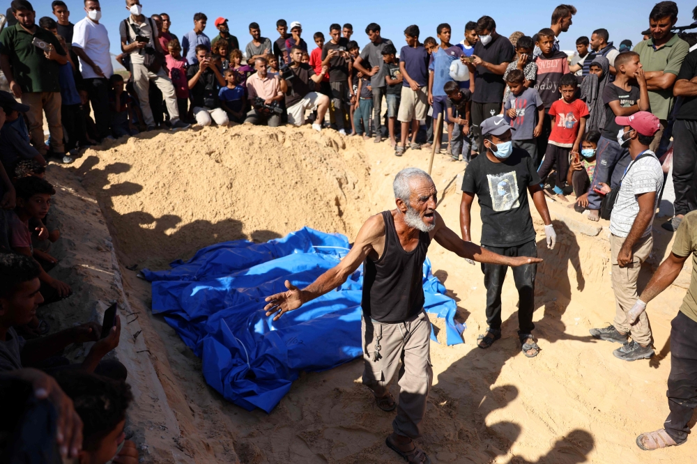 A man reacts as others gather to watch the burial of some of the 88 bodies in a mass grave in Khan Yunis on September 26, 2024. (Photo by Bashar Taleb / AFP)