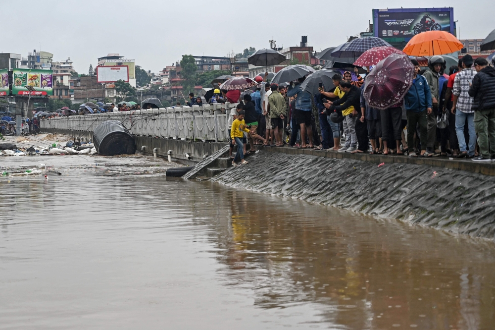 Residents stand along a street as they inspect flood waters after the Bagmati river overflowed during monsoon rains in Kathmandu on September 28, 2024. (Photo by Prakash Mathema / AFP)
 