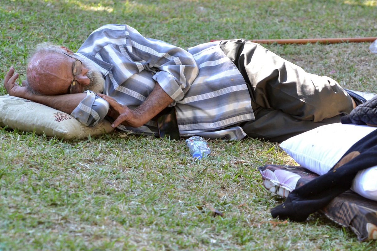 A man sleeps on the grass as displaced families who fled Israeli strikes in southern Lebanon gather at a park where they are taking refuge in Tripoli, on September 27, 2024. (Photo by Fathi Al-Masri / AFP)
