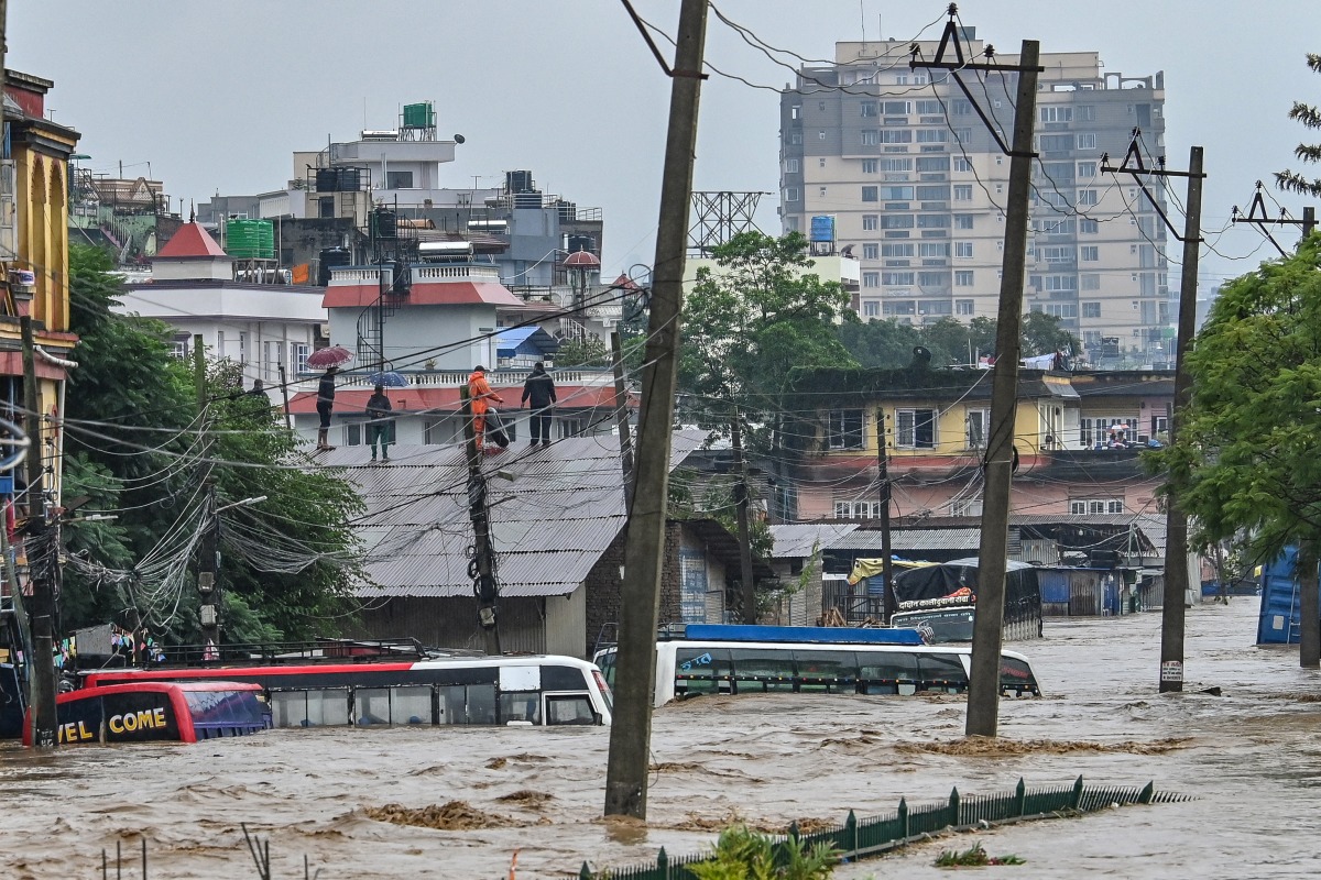 Residents climb over a rooftop as their neighbourhood submerged in flood waters in Kathmandu on September 28, 2024. (Photo by Prakash Mathema / AFP)