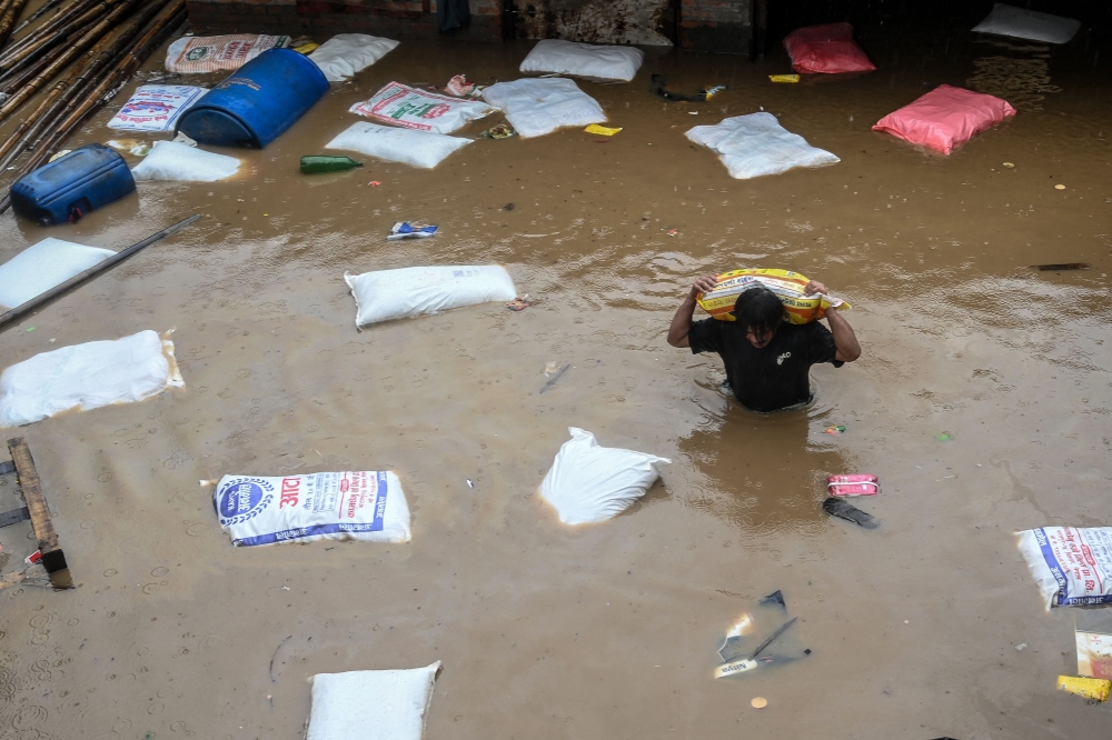 A man carrying a sack of flour wades through flood waters after the Bagmati River overflowed following heavy monsoon rains in Kathmandu on September 28, 2024. Photo by PRAKASH MATHEMA / AFP