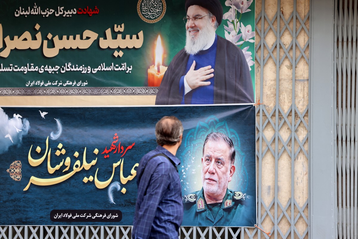 A man walks past banners in Tehran bearing pictures of slain Lebanese Hezbollah leader Hassan Nasrallah (top) and Iran's paramilitary Revolutionary Guard general Abbas Nilfrushan, two days after their targeted assassination by Israeli forces in Beirut's southern suburbs, on September 29, 2024. Photo by ATTA KENARE / AFP.