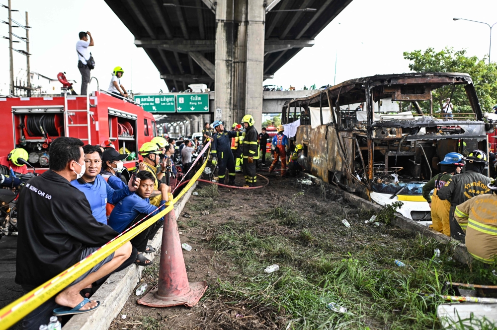 Firefighters and rescue workers stand next to a burnt-out bus that was carrying students and teachers on the outskirts of Bangkok, on October 1, 2024. (Photo by Manan VATSYAYANA / AFP)
