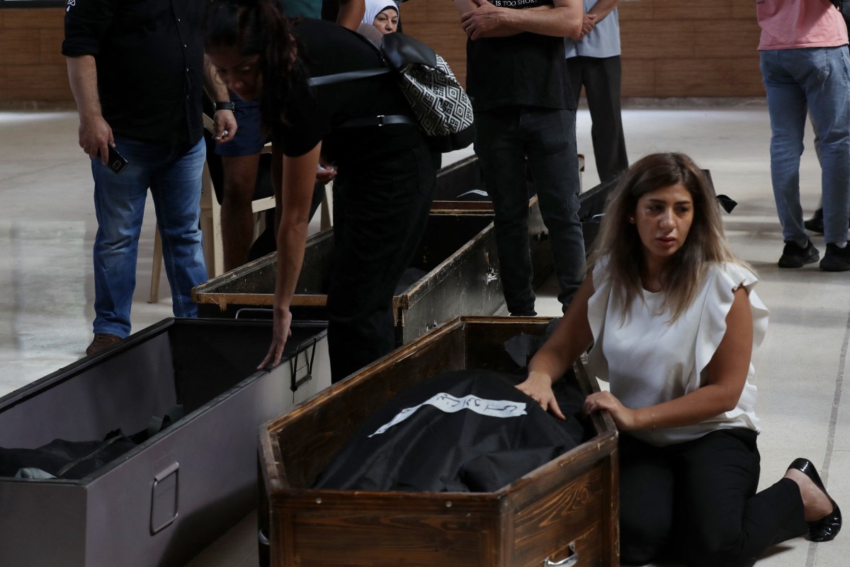 A woman mourns by the bodies of relatives killed on September 29 in an Israeli air strike on the town of Ain al-Delb, during their funeral in the nearby city of Sidon in southern Lebanon on October 1, 2024. Photo by Mahmoud ZAYYAT / AFP.