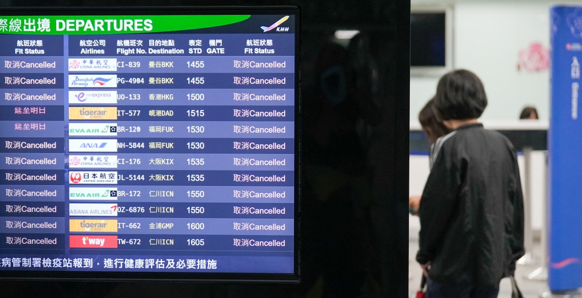 People stand next to a monitor showing flight status at Kaohsiung International Airport, with all flights cancelled as Typhoon Krathon nears in Kaohsiung on October 2, 2024. Photo by WALID BERRAZEG / AFP.