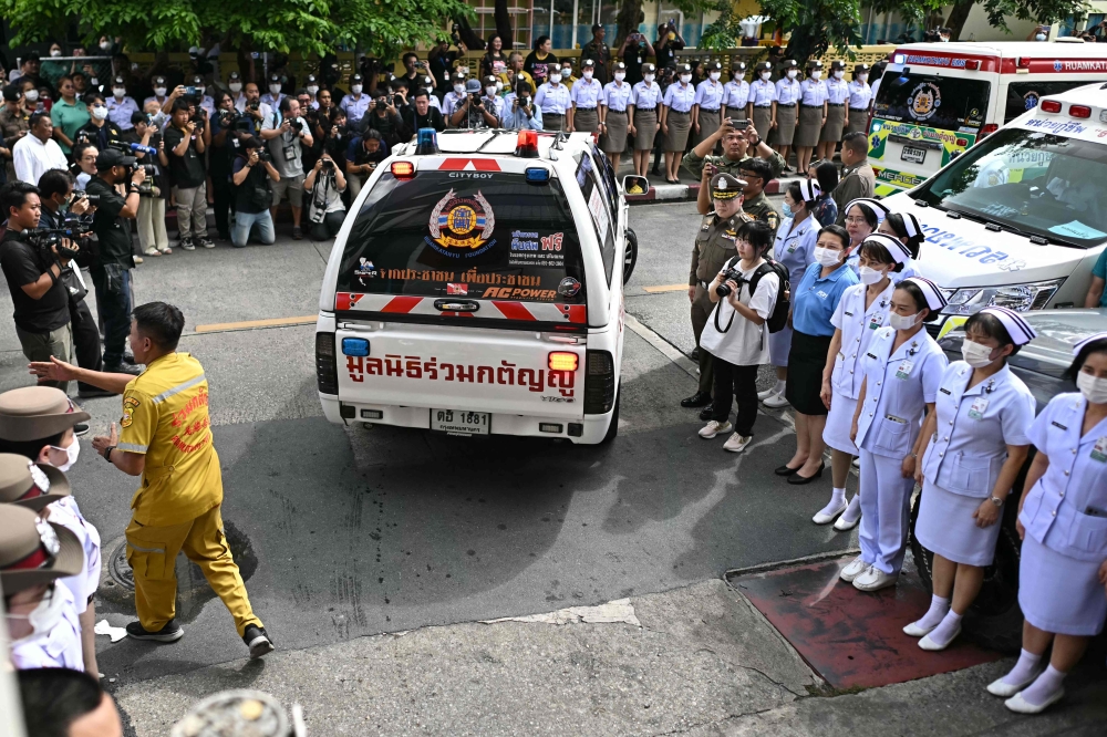 Police officers and nurses stand near media representatives as an ambulance carrying victims' remains leaves the forensic institute at the police hospital in Bangkok, on October 2, 2024. Photo by Manan VATSYAYANA / AFP