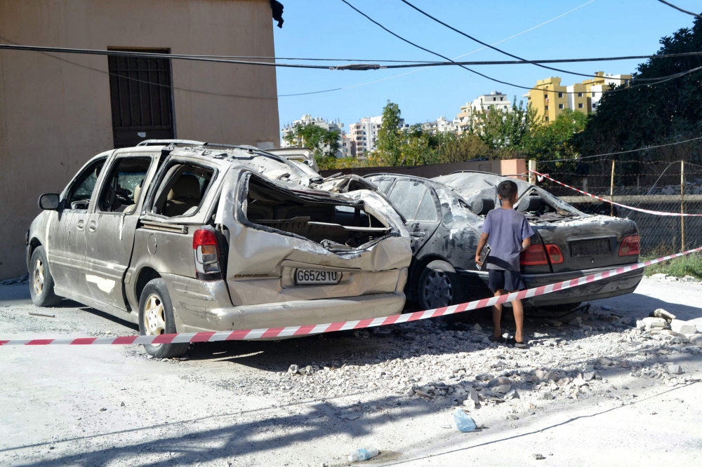 A child looks at damaged cars in a cordoned-off area hit in an Israeli airstrike that targeted an apartment building in the Palestinian refugees camp of Al-Baddawi near the northern Lebanese city of Tripoli on October 5, 2024. (Photo by Fathi Al Masri / AFP)