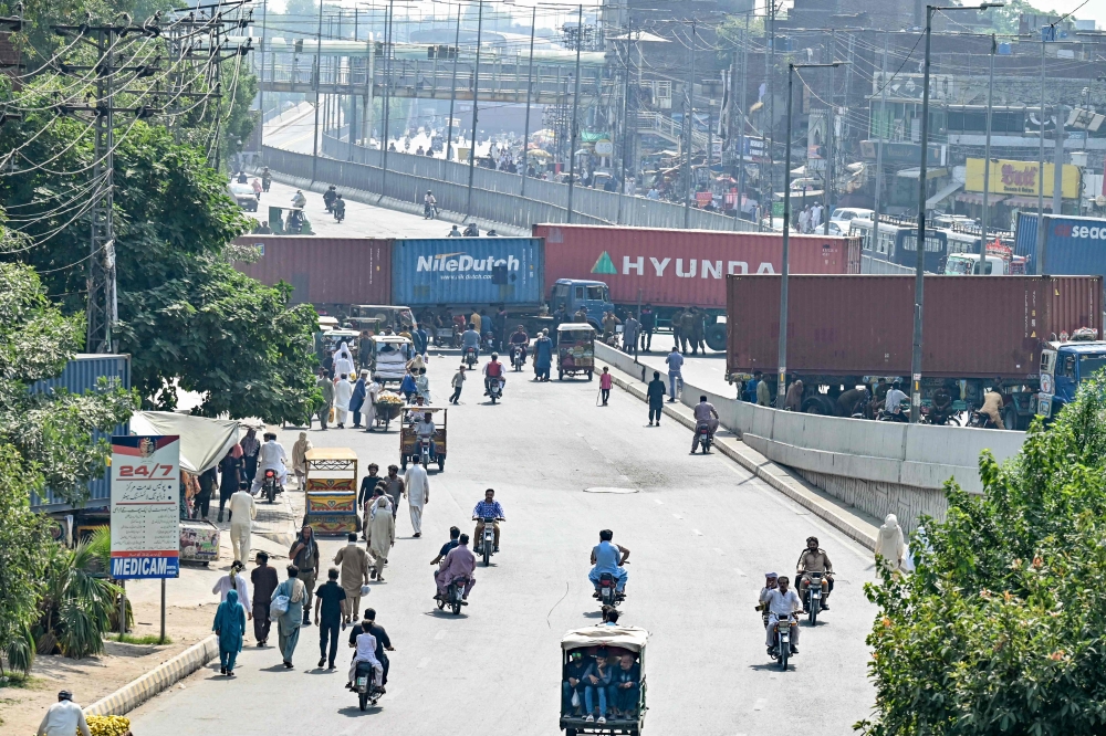 Commuters trace back from a street blocked with shipping containers by authorities for security measures against a protest in Lahore on October 5, 2024. (Photo by Arif Ali / AFP)