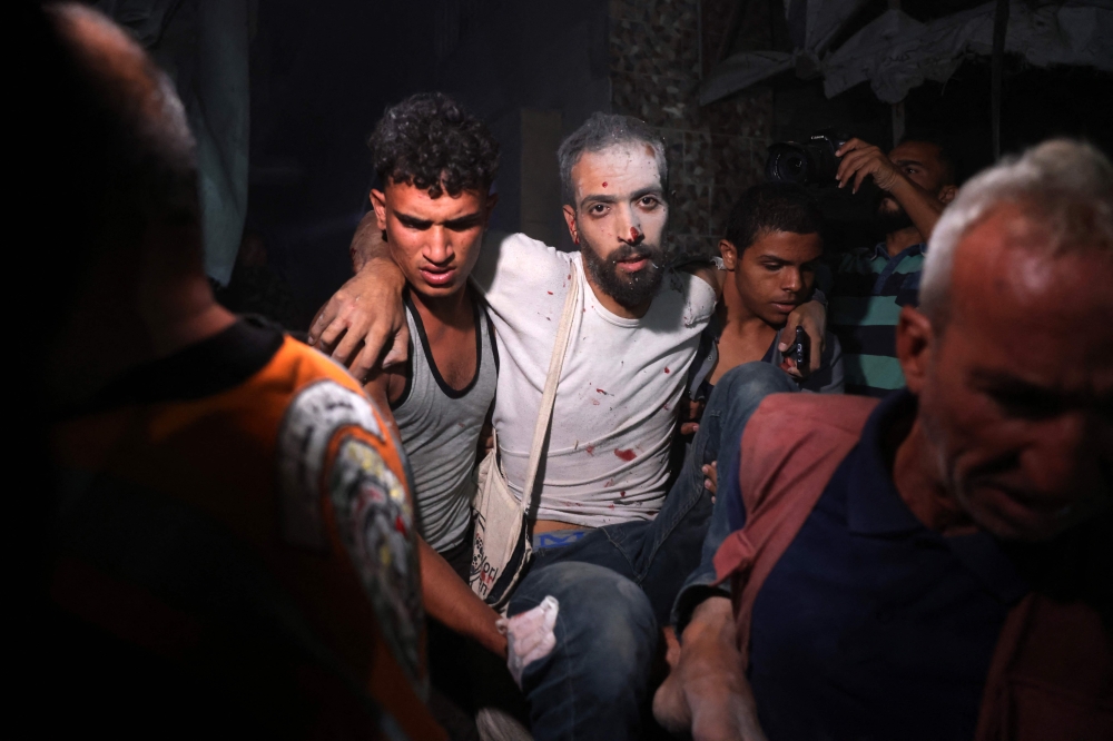 Palestinians help a man injured in an Israeli strike that targeted a mosque-turned-shelter in Deir al-Balah in the central Gaza Strip. (Photo by Bashar Taleb / AFP)