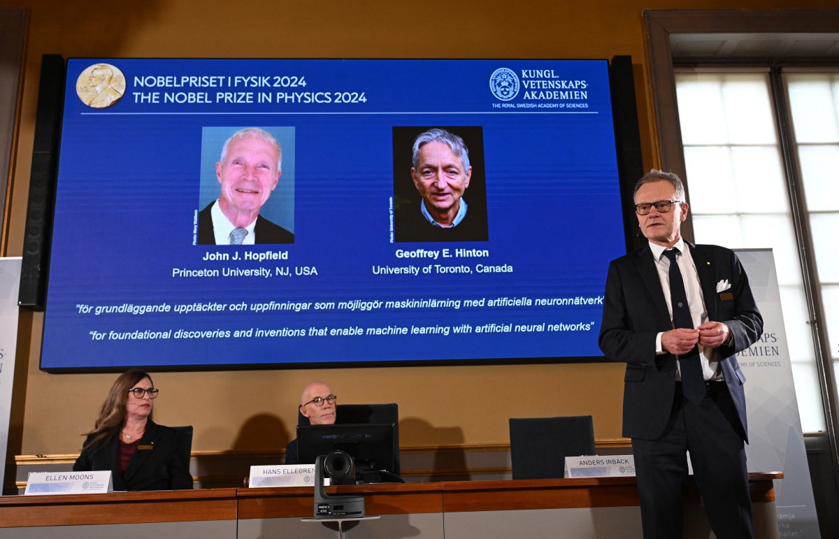 A screen shows the laureates of the 2024 Nobel Prize in Physics, US physicist John J Hopfield and Canadian-British computer scientist and cognitive psychologist Geoffrey E Hinton as member of the Nobel Committee for Physics Anders Irbaeck (R) delivers a speech following the announcement at the Royal Swedish Academy of Sciences in Stockholm, Sweden on October 8, 2024.
Photo by Jonathan NACKSTRAND / AFP.