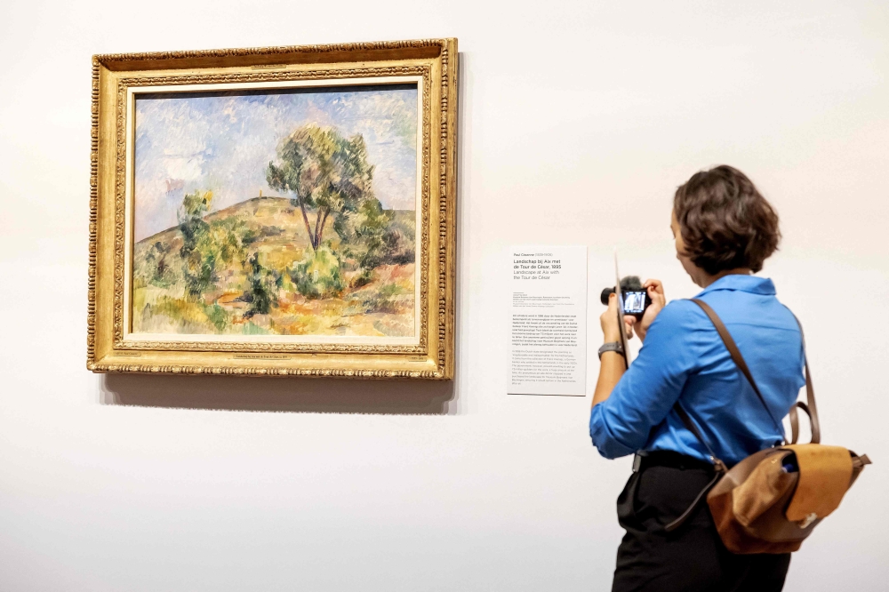 A woman looks at the work 'Landscape near Aix with Tour de Cesar' by Paul Cezanne from the new exhibition 'Vive l'impressionnisme!' at the Van Gogh Museum in Amsterdam on October 9, 2024. (Photo by Robin van Lonkhuijsen / ANP / AFP)