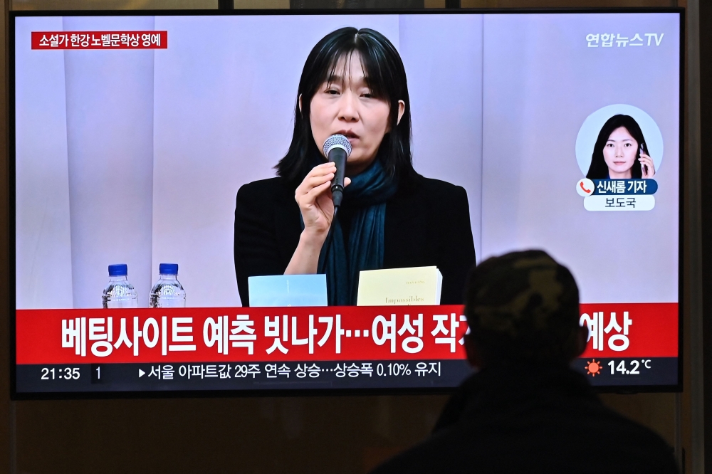 A person watches a news broadcast with file footage of South Korean author Han Kang, at a train station in Seoul on October 10, 2024. Photo by JUNG YEON-JE / AFP