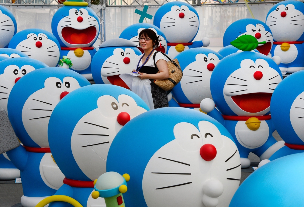 This picture taken on July 18, 2013 shows a journalist walking amid life-size figures of Doraemon during the press preview of the Fujiko F Fujio Exhibition in Tokyo. Photo by TORU YAMANAKA / AFP