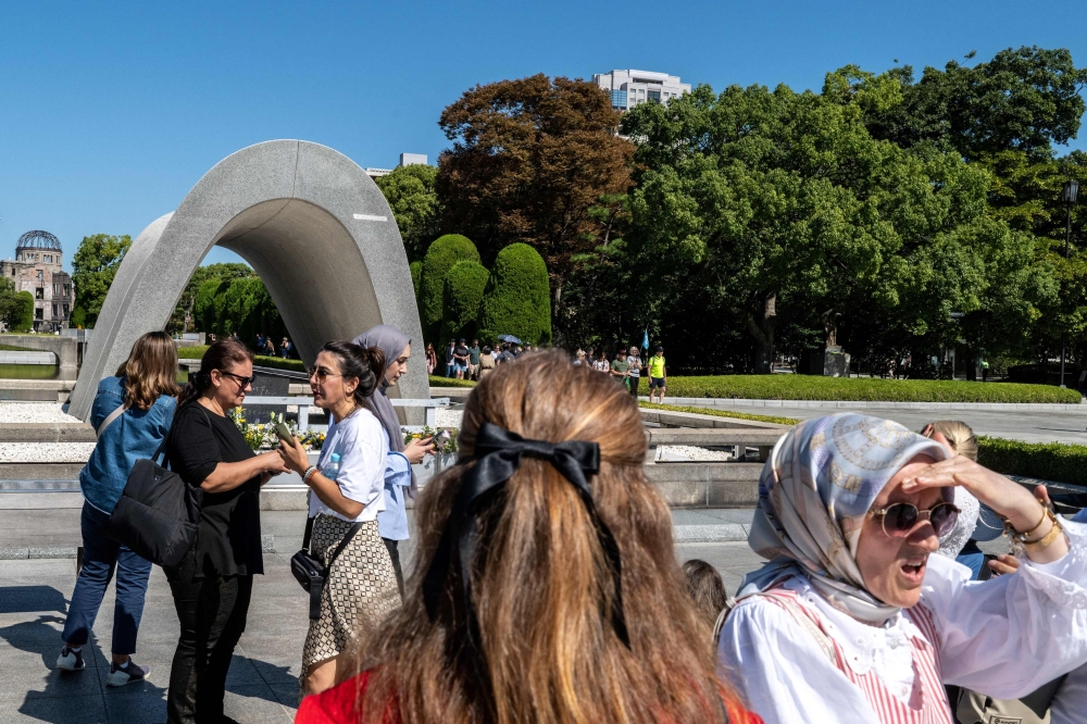 A group of tourists visits the cenotaph as the ruins of the Hiroshima Prefectural Industrial Promotion Hall, now commonly known as the atomic bomb dome (back), is seen from the Hiroshima Peace Memorial Park in Hiroshima city on October 12, 2024. (Photo by Philip FONG / AFP)