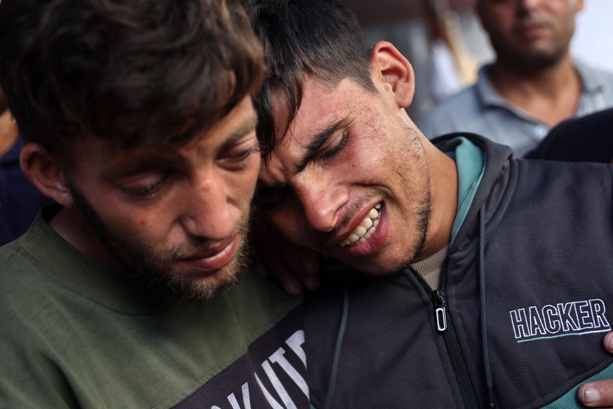 Ali Assaf (R), 20, reportedly the only survivor from his family killed in an overnight Israeli airstrike in the Jabalia refugee camp in the northern Gaza Strip, is comforted by a young man as mourns near the bodies of his relatives in front of the al-Maamadani on October 12, 2024. Photo by Omar AL-QATTAA / AFP.
