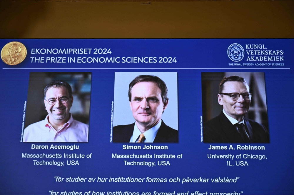 A screen shows the laureates (L-R) Turkish-American Daron Acemoglu and British-Americans Simon Johnson and James Robinson of the 2024 Sveriges Riksbank Prize in Economic Sciences in Memory of Alfred Nobel during the announcement by the Royal Swedish Academy of Sciences in Stockholm, Sweden on October 14, 2024. (Photo by Christine Olsson / TT NEWS AGENCY / AFP) 