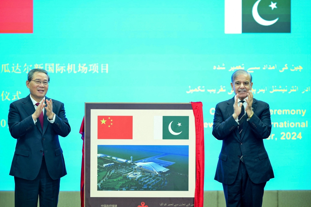 In this handout photograph taken on October 14, 2024, and released by Pakistan's Prime Minister Office, China's Premier Li Qiang (L) and Pakistan's Prime Minister Shehbaz Sharif gesture after unveiling a plaque to mark the completion of New Gwadar International Airport (NGIA) during a ceremony at the Prime Minister House in Islamabad. (Photo by Pakistan's Prime Minister Office / AFP) 