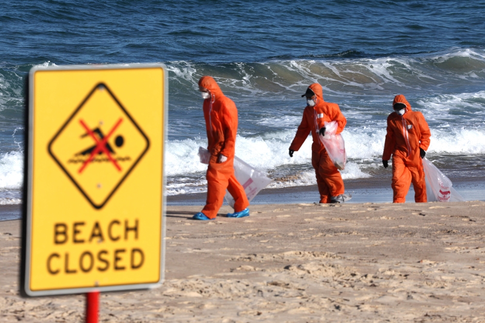 Workers in protective suits conduct a cleanup operation to clear petroleum-based 